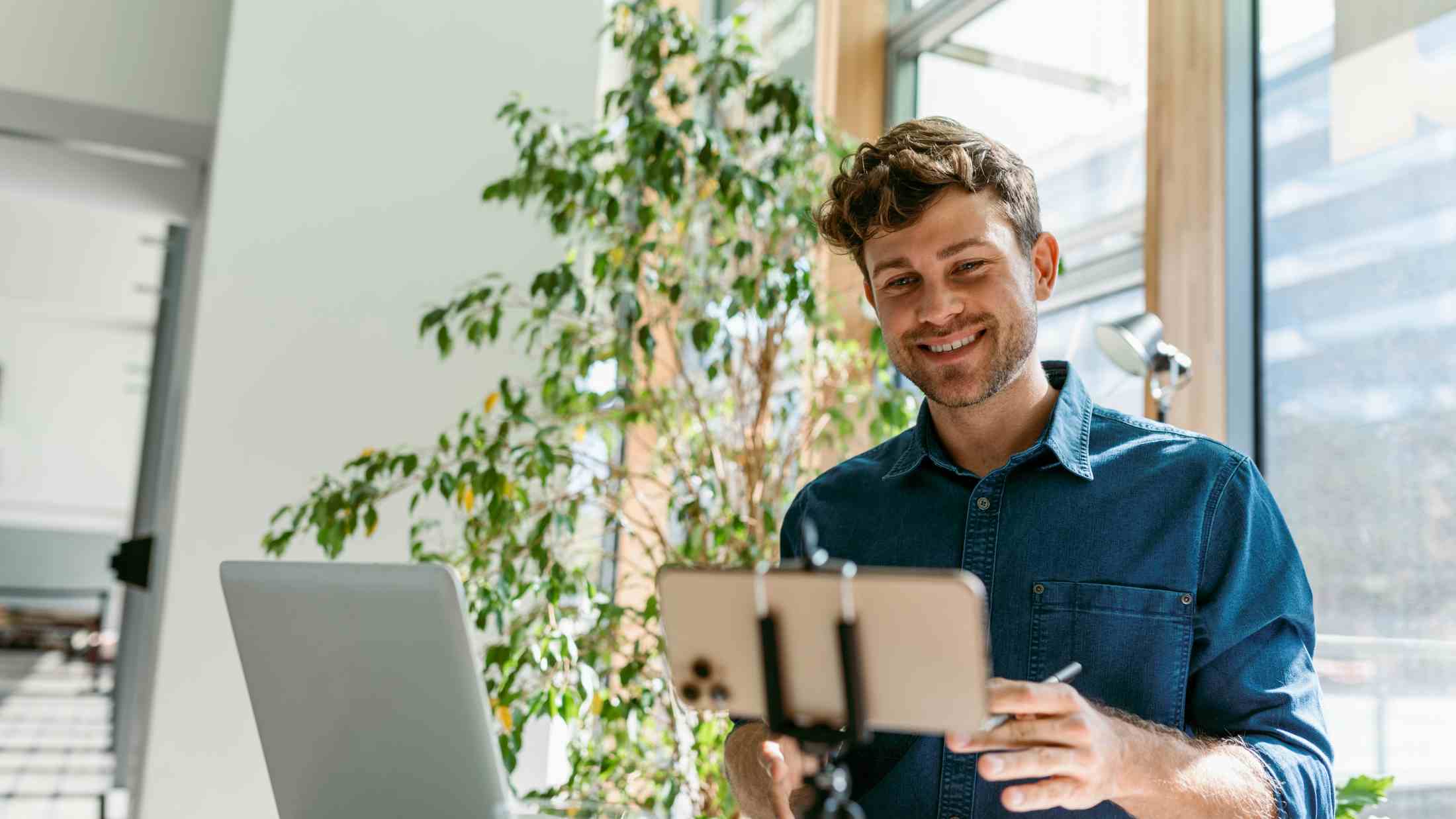 Man smiling while looking at a laptop and phone